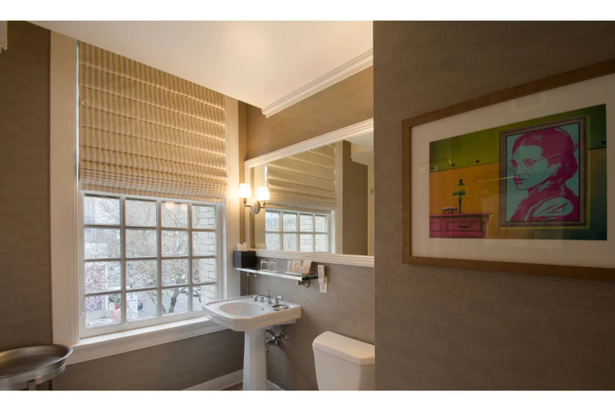 This image shows a modern suite interior featuring a well-lit vanity area with a sink and mirror, a window letting in natural light, and framed artwork that reflects the artistic spirit of Portland. The space is uncluttered and accessible, suggesting thoughtful consideration of mobility and ease of use.