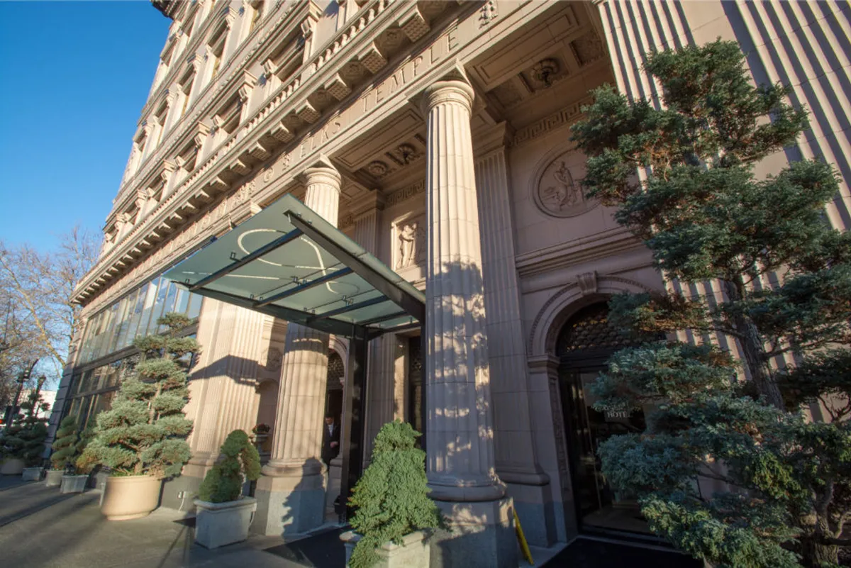 A welcoming view of the hotel’s grand exterior, featuring ornate columns, a modern glass awning, and topiary plants flanking the entrance. The scene captures the blend of classic and contemporary elements that define the hotel’s presence in downtown Portland.