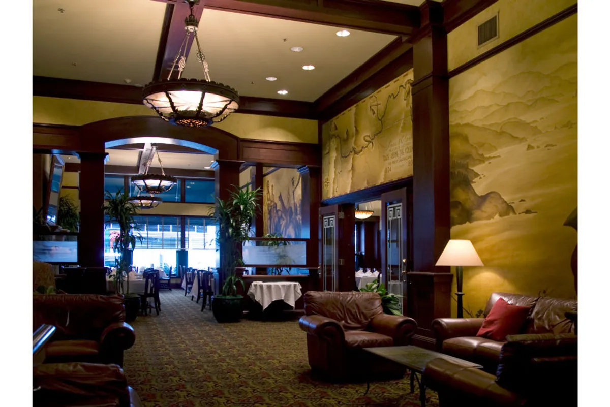 A sophisticated corner with ornate chandeliers, leather sofas, a decorative mural, and potted plants. The cozy arrangement encourages guests to relax, catch up on shows, or enjoy music in a stylish environment.