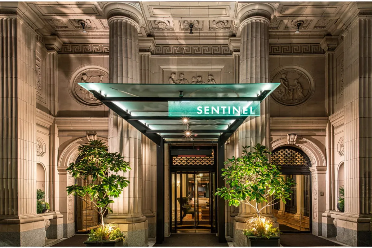 A sophisticated exterior shot of the hotel's entrance, featuring an illuminated sign, entrance canopy, and detailed architectural flourishes. The scene exudes a welcoming and luxurious ambiance, hinting at the high-end experiences found both inside and nearby.