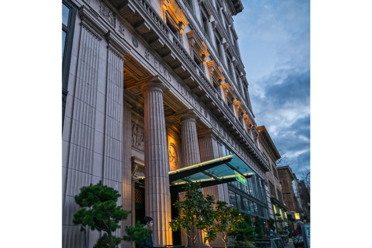 An exterior view highlighting the ornate columns, illuminated entrance, and decorative facade of the building. The setting suggests a vibrant atmosphere suited for dining outdoors, social gatherings, and people-watching, with hints of the city's cultural and culinary vibrancy.