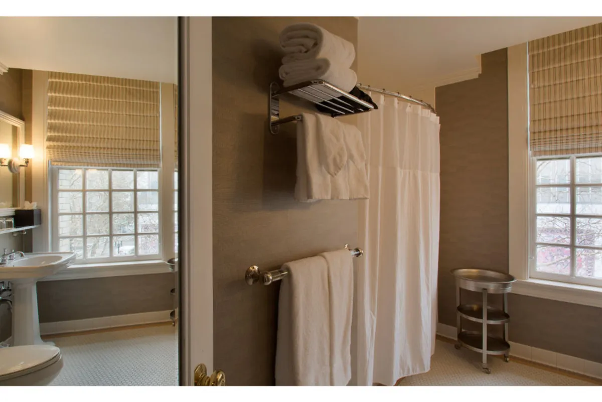 A serene bathroom scene with a shower curtain, accessible sink, ample towels, and a window providing natural light. The layout and fixtures hint at mobility-friendly features, contributing to a sense of ease and relaxation.