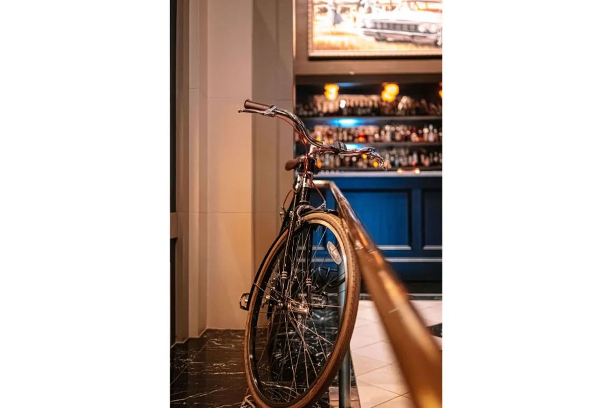 A stylish, inviting lounge area with a bicycle on display, a bar counter, and distinctive lighting fixtures. The setting is lively and welcoming, suggesting opportunities for guests to socialize, relax, and enjoy local culture, possibly after exploring the city.
