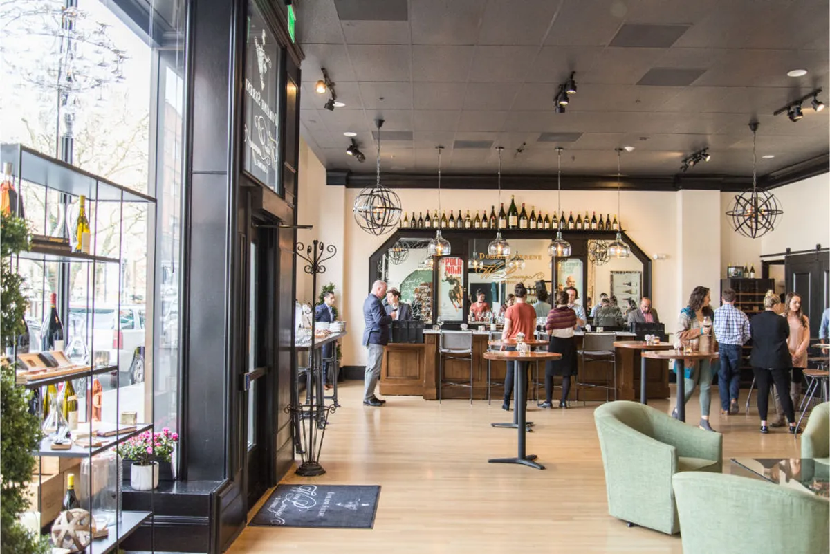 A lively bar area featuring a modern seating arrangement, display shelves filled with bottles, and an inviting atmosphere. The space is well-lit and designed for social gatherings, wine tasting events, and casual dining.